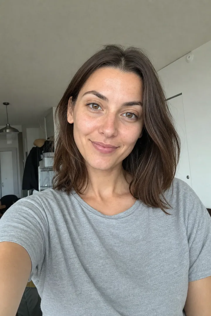 An ordinary phone selfie of a woman in a gray T-shirt at home